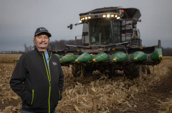 Tom Neufeld stands in front of his farming equipment in a field.